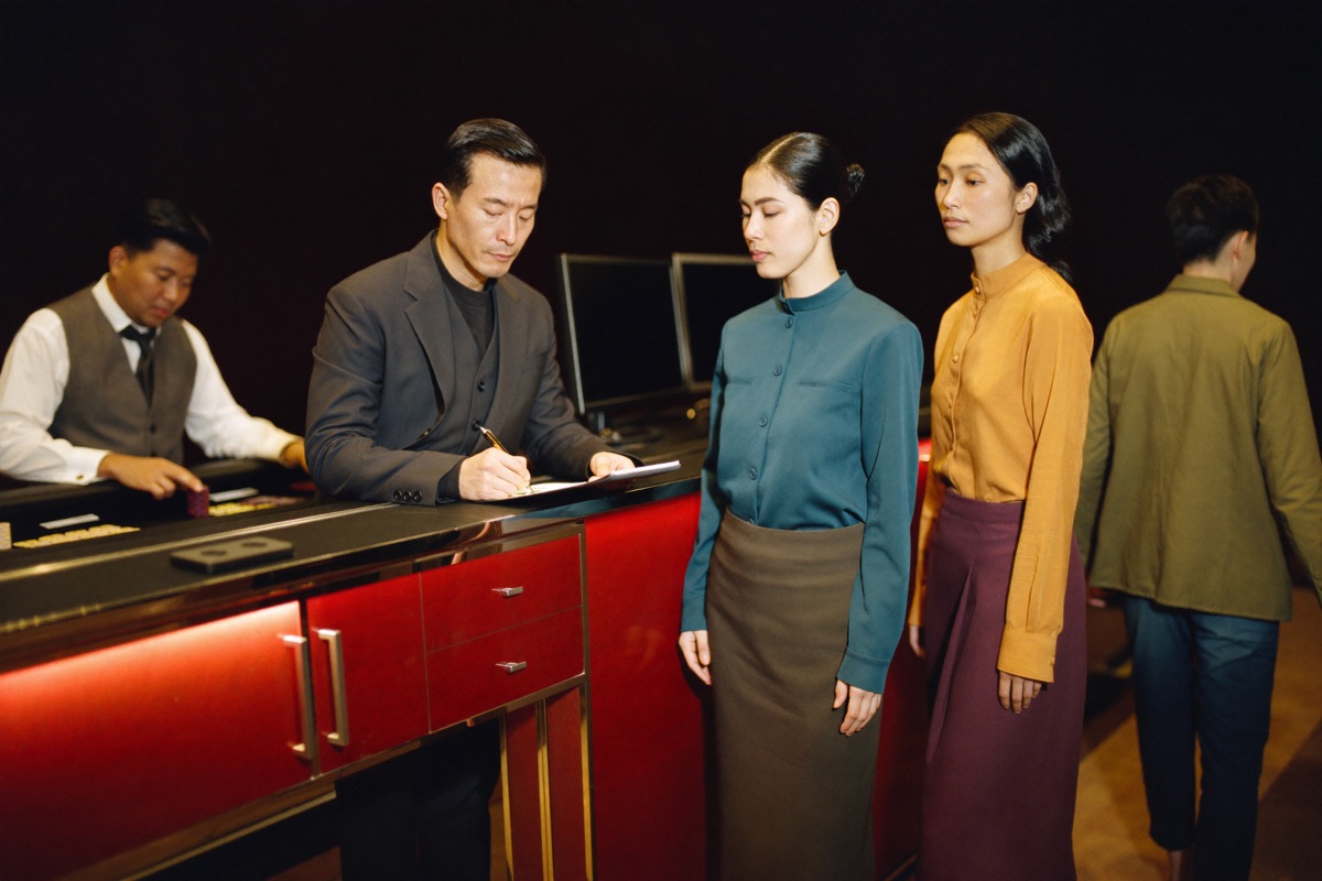 A floor supervisor in a dark suit at a raised pit desk with a dealer at a table on either side of him