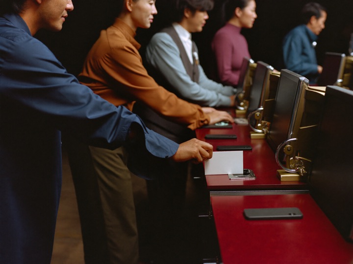 A row of three slot cabinets seen straight on with a card reader lit on the middle one and a hand resting a plain blank card against the reader plate
