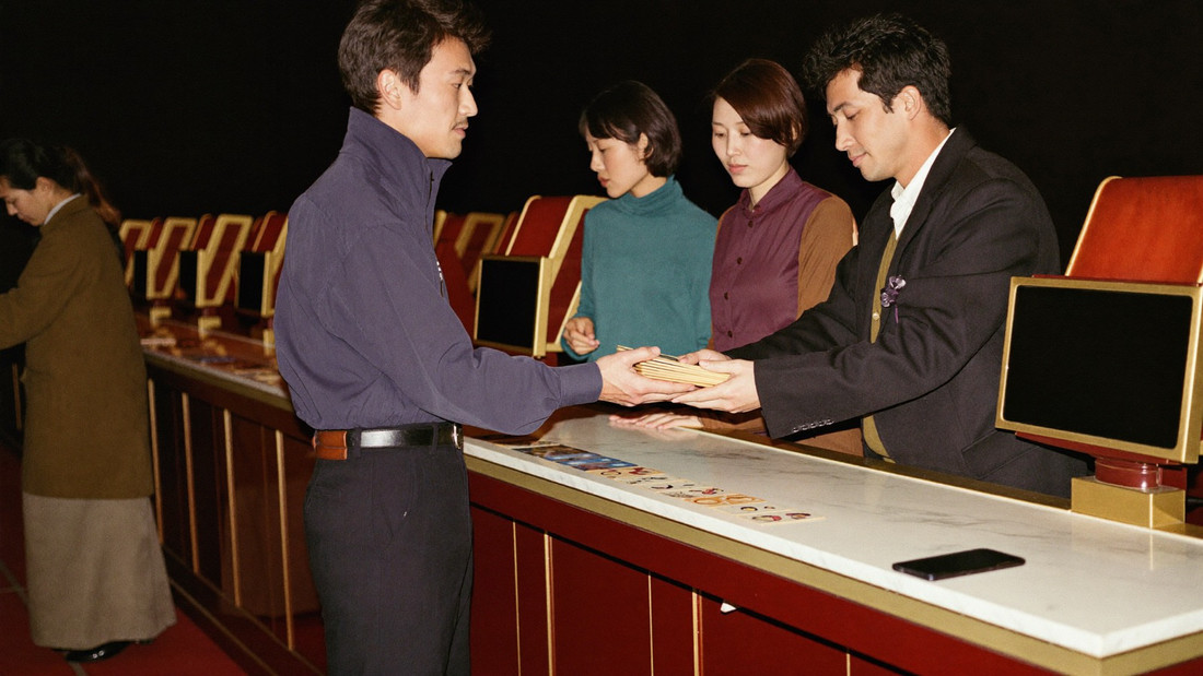 A cashier in a waistcoat sliding a neat stack of gaming plaques across a marble counter into a player's open hand
